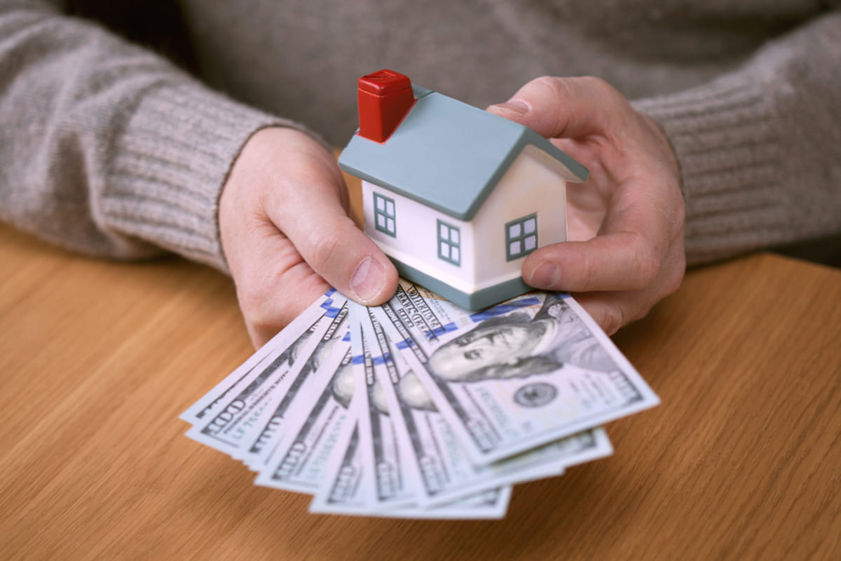 Close-up of hands holding cash and a model house, buy my house for cash concept