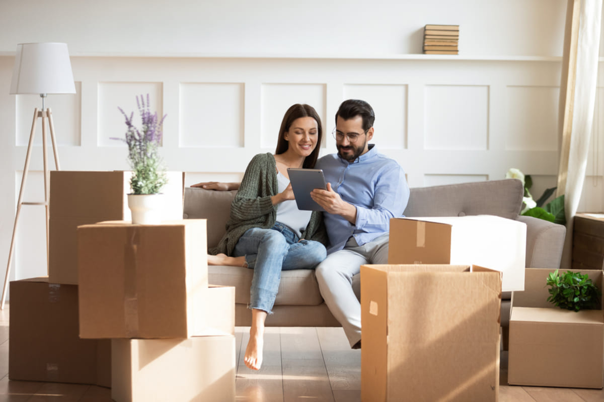 Happy couple sitting on a couch surrounded by moving boxes