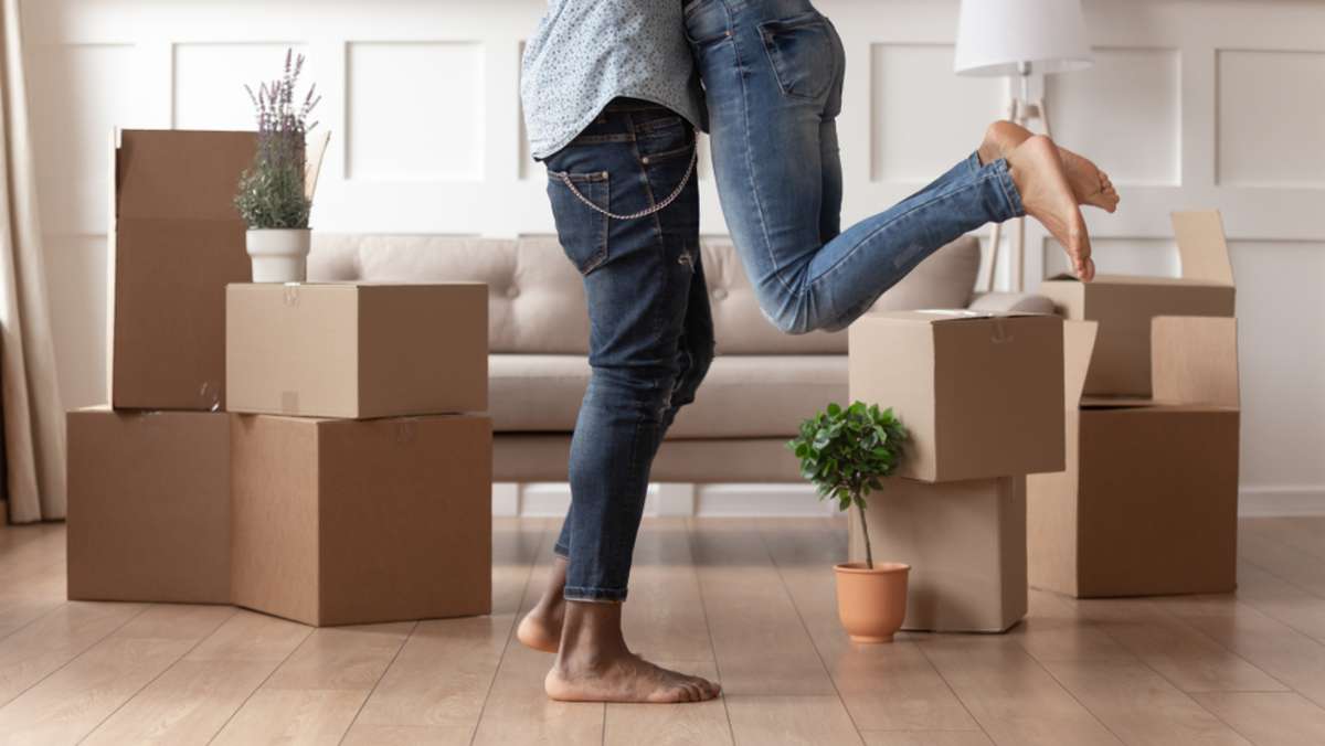 Close up young husband in jeans lift wife surrounded by cardboard boxes excited to move in new flat