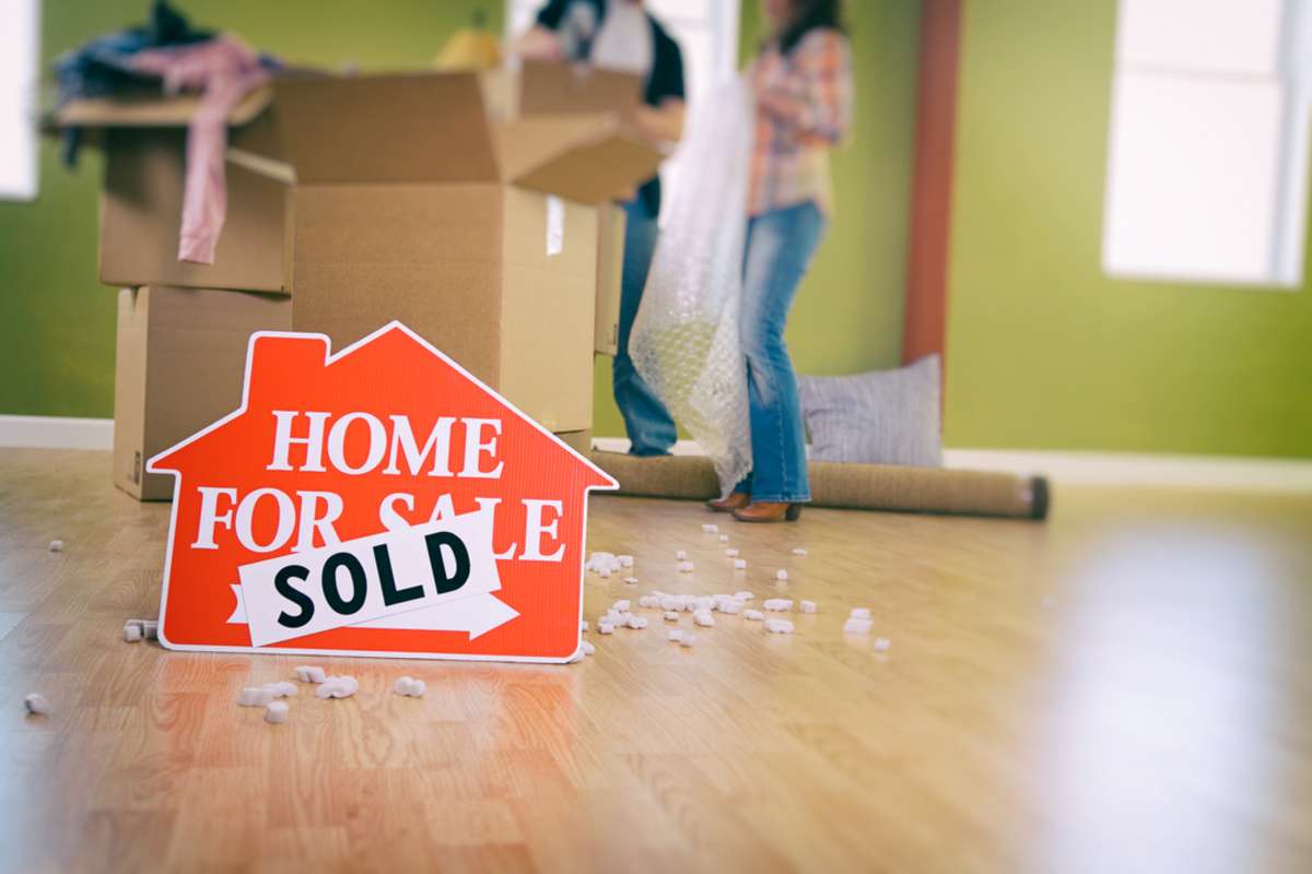 Couple packing with Sold sign in the foreground, companies that buy houses for cash concept.