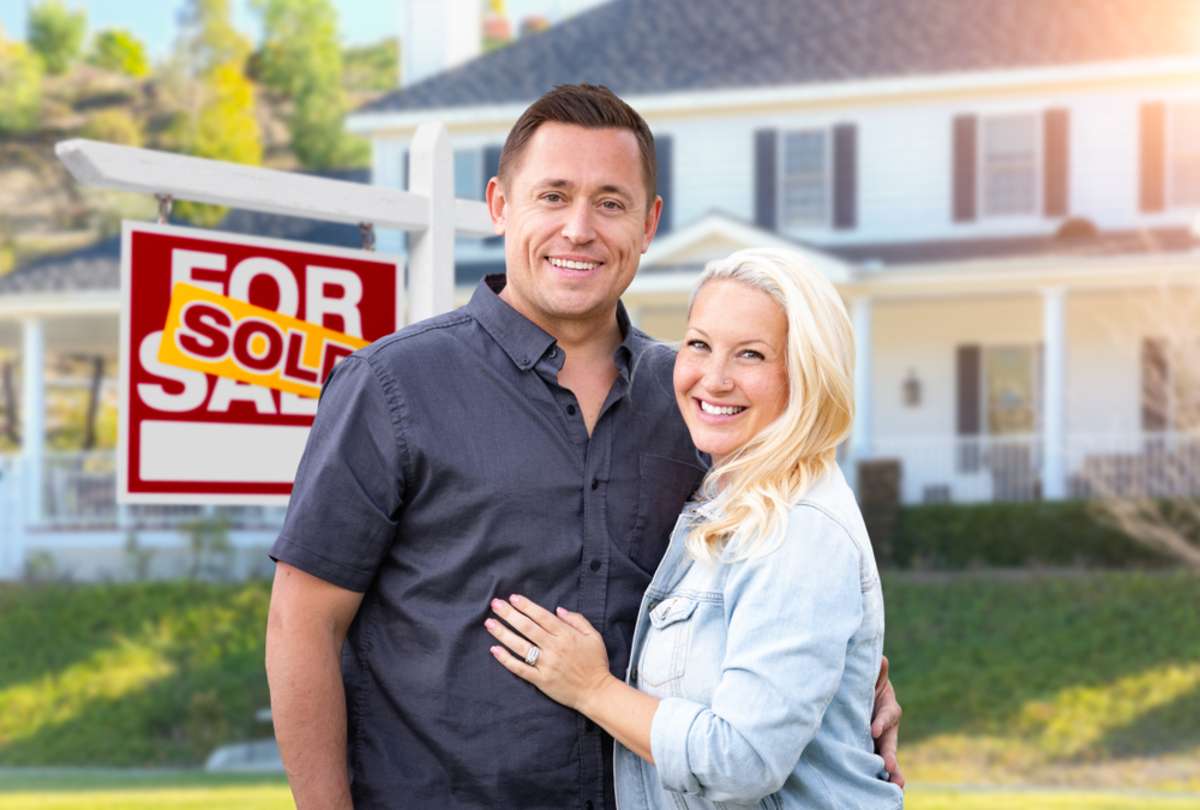 Happy Couple In Front of Sold Real Estate Sign and Beautiful House