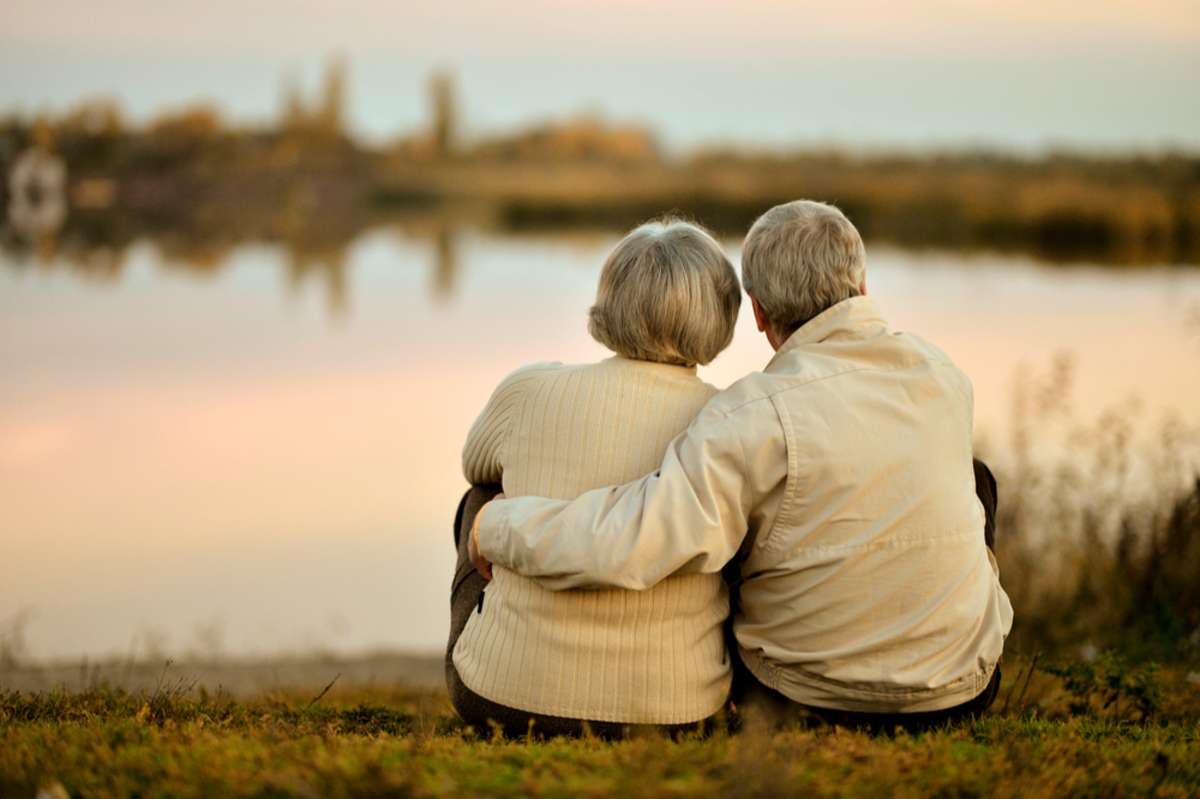 Happy senior couple sitting in summer near lake during sunset, inherited properties concept. 