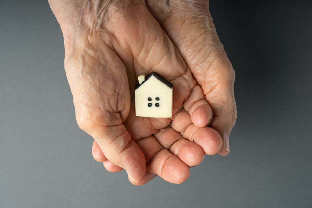 Inheritance concept. Elderly woman hands holds a little toy house
