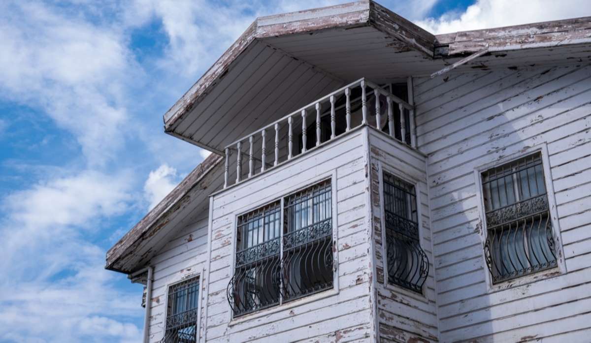 Old white wooden house, worn white building need restoration, roof top and blue sky