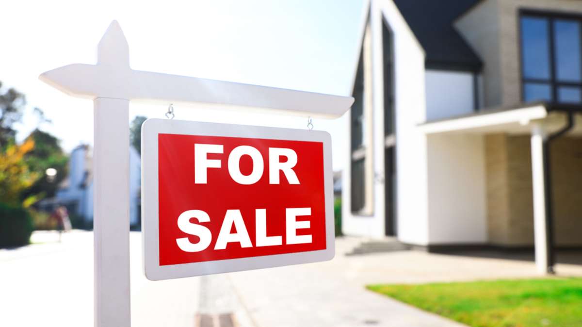 Red real estate sign near house outdoors on sunny day