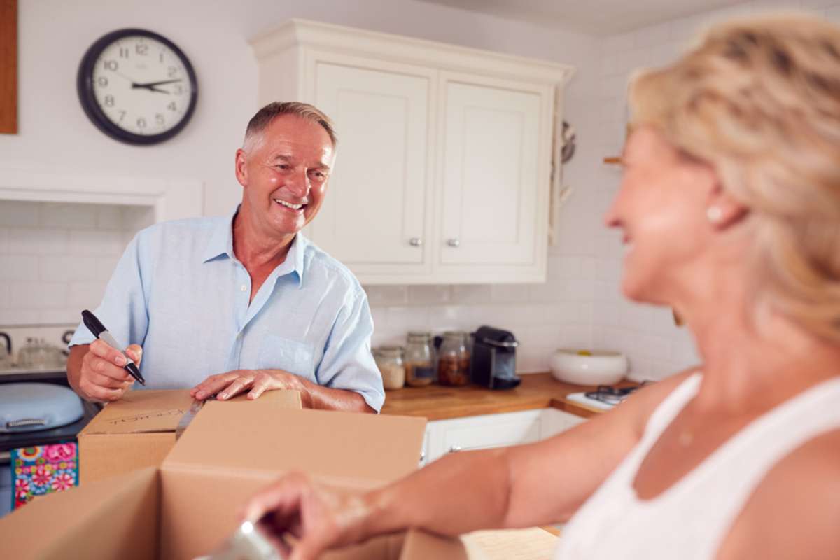 Senior Couple Downsizing In Retirement Packing And Labelling Boxes Ready For Move Into New Home