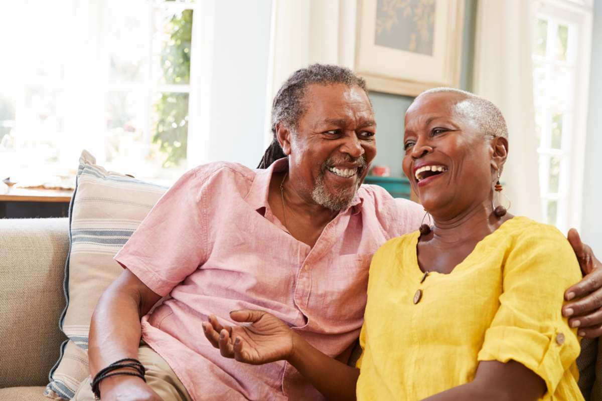 Smiling Senior Couple Sitting On Sofa At Home Together