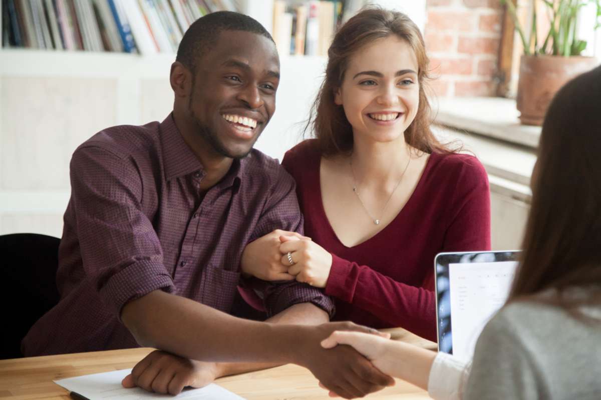 Smiling couple shaking hands with a person representing cash home buying companies.