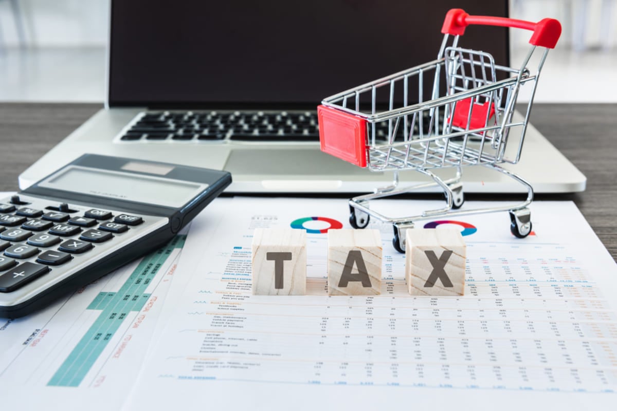 The word tax spelled by wooden blocks next to shopping cart and charts